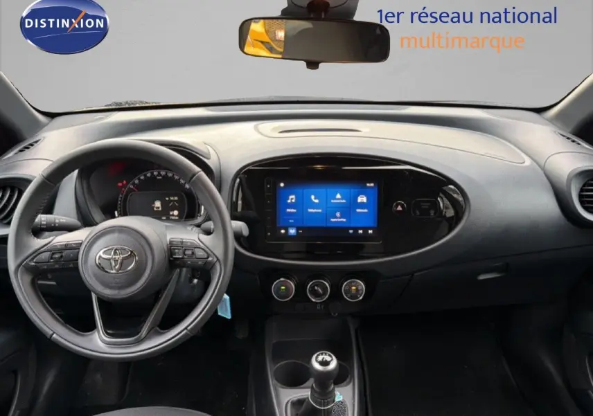 Vue intérieure frontale du tableau de bord noir de la Toyota Aygo X 2025 avec écran tactile et boîte manuelle.