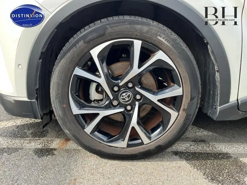 Gros plan sur la roue avant droite du Toyota C-HR blanc nacré bi-ton avec jante alliage noire et argentée.