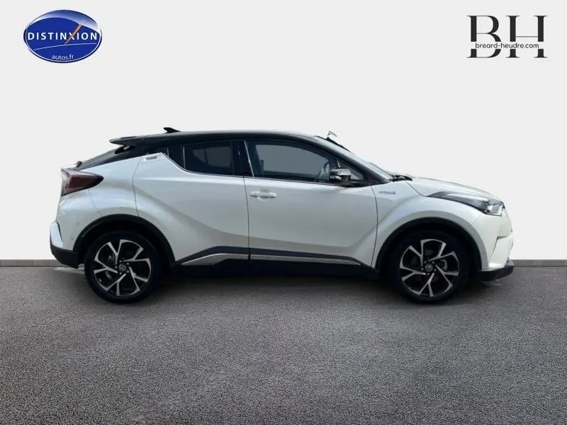 Toyota C-HR 122h Collection 2WD blanc nacré bi-ton vu de profil côté gauche avec jantes alu noires et toit noir.