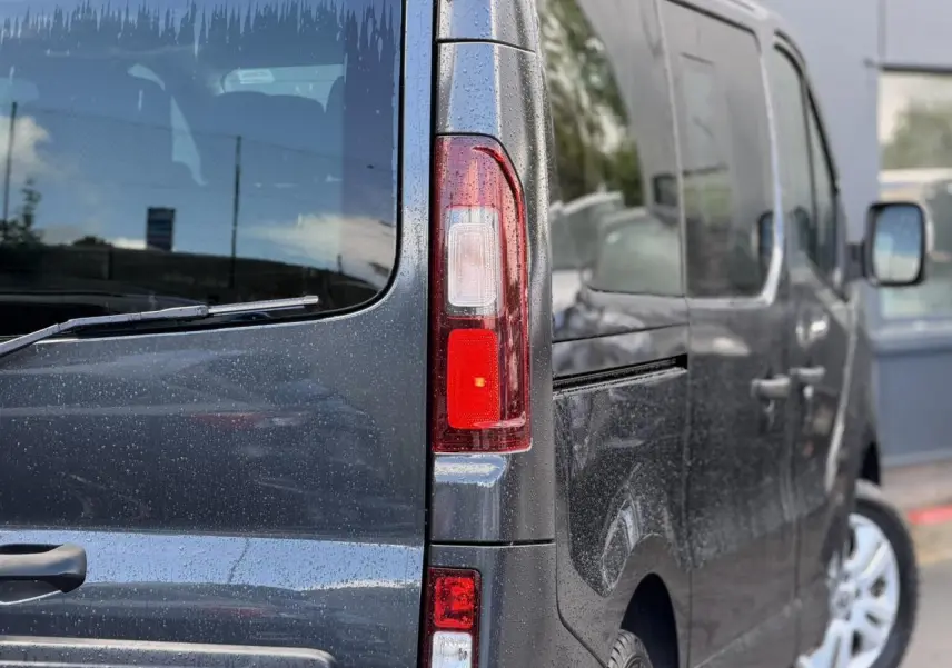 Vue arrière gauche rapprochée du Nissan Primastar gris comète avec hayon vitré et feux arrière allongés.