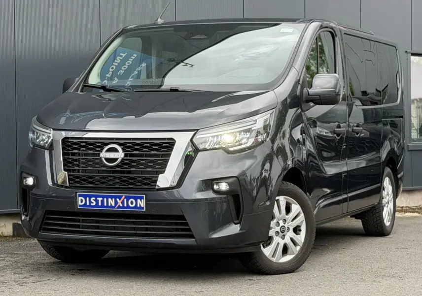 Nissan Primastar gris Comète en 3/4 avant droit, avec calandre chromée et phares LED allumés.