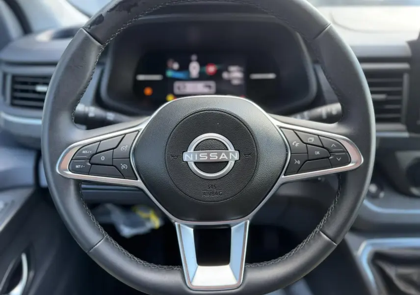 Vue rapprochée du volant noir du Nissan Primastar 2025 avec commandes intégrées et logo central argenté.