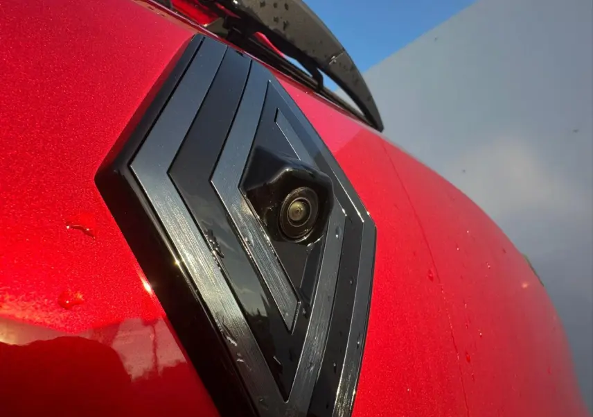 Gros plan sur le logo Renault noir brillant avec caméra intégrée sur la calandre rouge foncé de la Clio V Alpine.