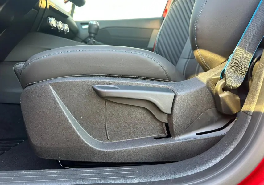Détail de l'accoudoir avant coulissant côté gauche avec sellerie noire et surpiqûres bleues sur Renault Clio rouge foncé.