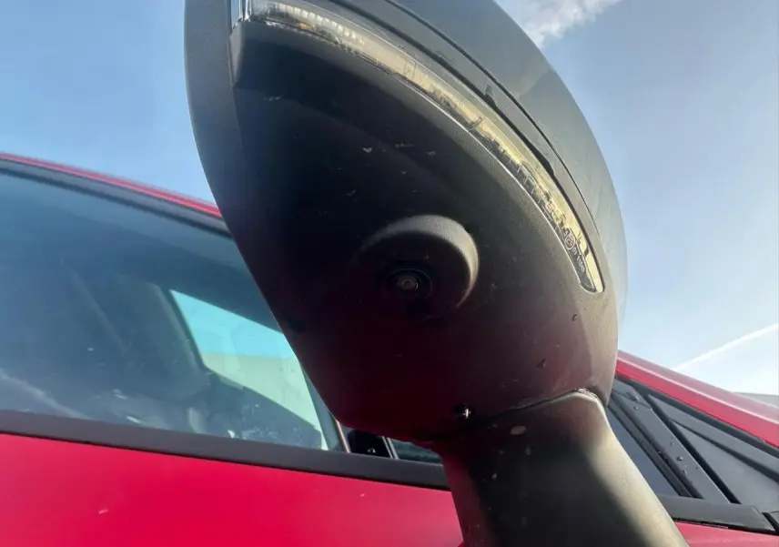 Gros plan sur le rétroviseur droit noir brillant avec caméra, sur Renault Clio rouge foncé vue côté droit.