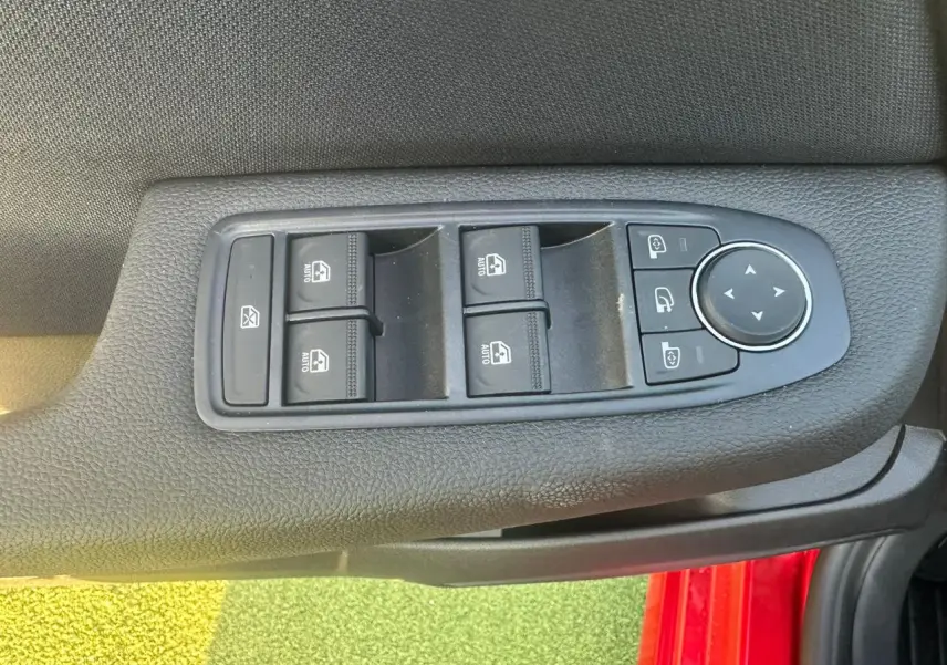 Détail des commandes des vitres et rétroviseurs sur la porte côté conducteur d’une Renault Clio rouge foncé.