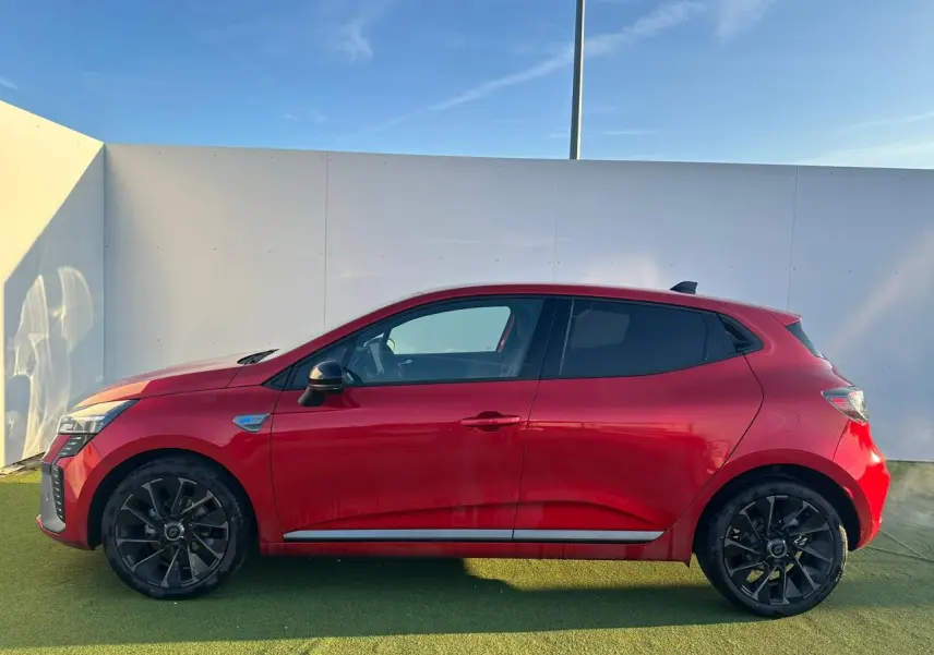Profil droit de la Renault Clio V rouge foncé avec jantes noires et badges esprit Alpine visibles sur ailes avant.