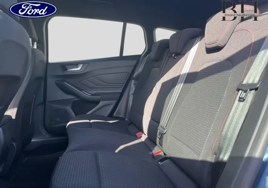 Vue latérale droite de l’intérieur arrière de la Ford Focus SW 2024 avec sièges tissu noir et surpiqûres rouges.