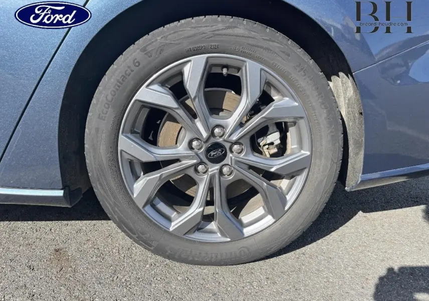 Gros plan sur la roue avant gauche avec jante alu grise du Ford Focus SW bleu azur métallisé 2024.