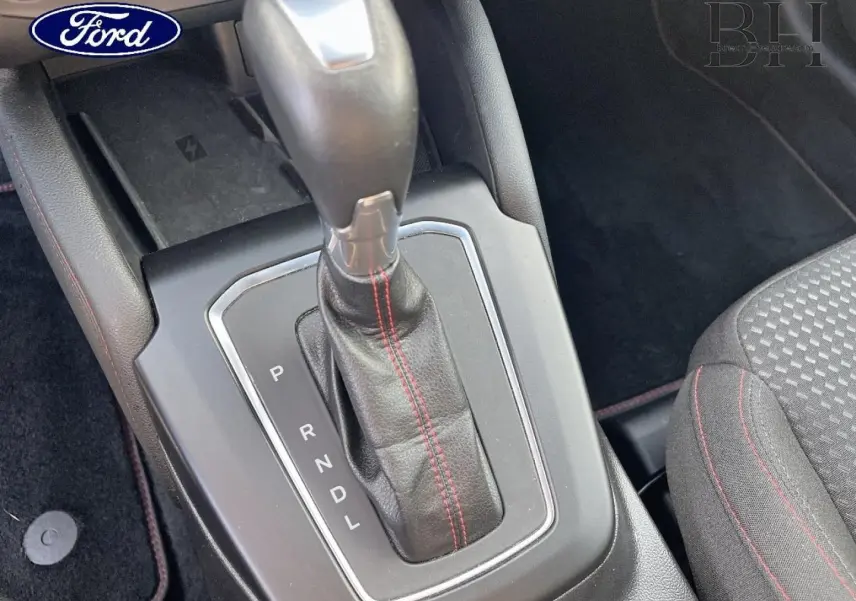 Gros plan sur le levier de vitesses automatique avec surpiqûres rouges, console centrale et siège tissu noir à surpiqûres rouges Ford Focus SW.