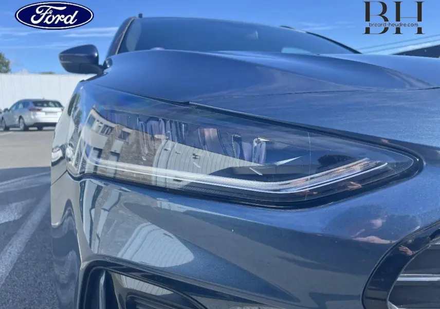 Gros plan sur le phare avant gauche bleu azur métallisé de la Ford Focus SW 2024, soulignant ses lignes modernes et épurées.