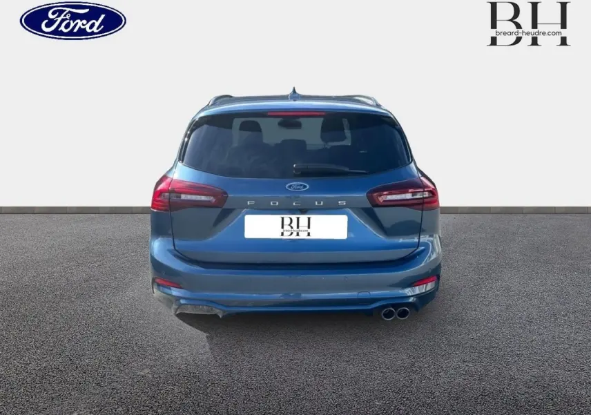 Vue arrière d'une Ford Focus SW 2024 bleu azur métallisé avec double sortie d'échappement chromée et feux LED.