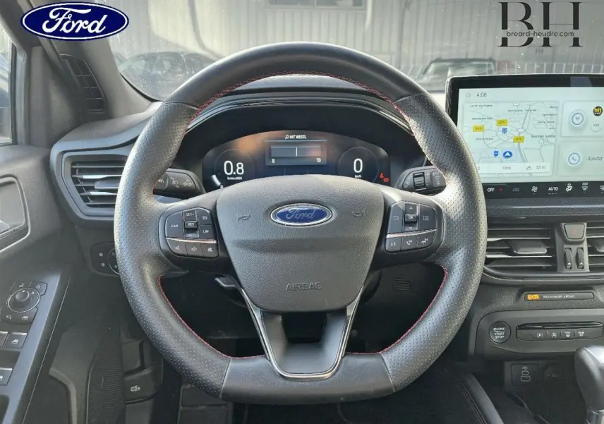 Vue centrée sur le volant cuir perforé avec surpiqûres rouges et tableau de bord numérique de la Ford Focus SW 2024.