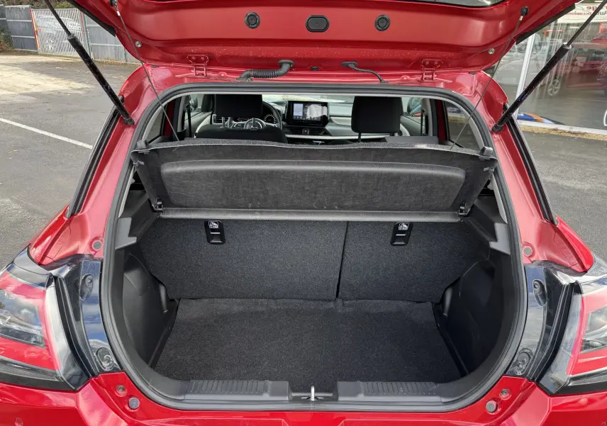 Coffre ouvert vu de l'arrière d'une Suzuki Swift rouge Burning Red Pearl Metal, intérieur noir et tableau de bord visible.