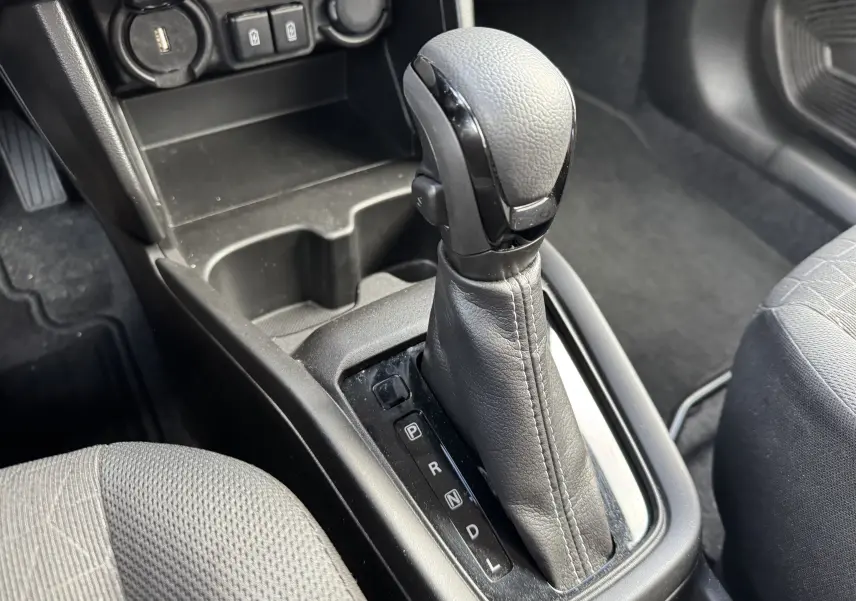 Gros plan sur le levier de vitesse automatique noir et gris de la Suzuki Swift 1.2 Hybrid Privilege 2025, intérieur sombre.