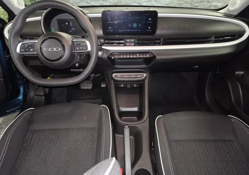 Vue intérieure avant de la FIAT 600 Hybrid 2024 avec tableau de bord noir mat et écran tactile central.