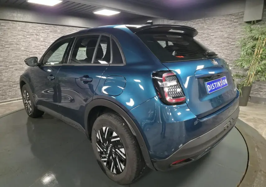 Vue 3/4 arrière droite d'une FIAT 600 hybride bleu métallisé avec jantes bicolores et feux arrière LED dans un showroom.