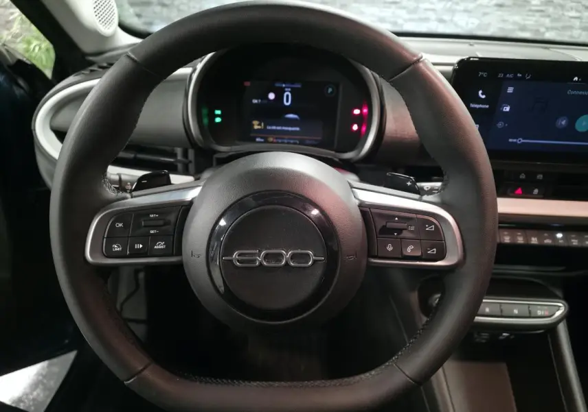 Vue intérieure centrée sur le volant noir de la Fiat 600 1.2 Hybrid 2024 avec tableau de bord numérique et écran tactile.