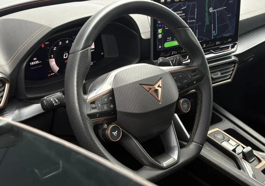 Vue rapprochée du volant cuir noir perforé avec logo CUPRA cuivré et tableau de bord digital du Leon 2025.