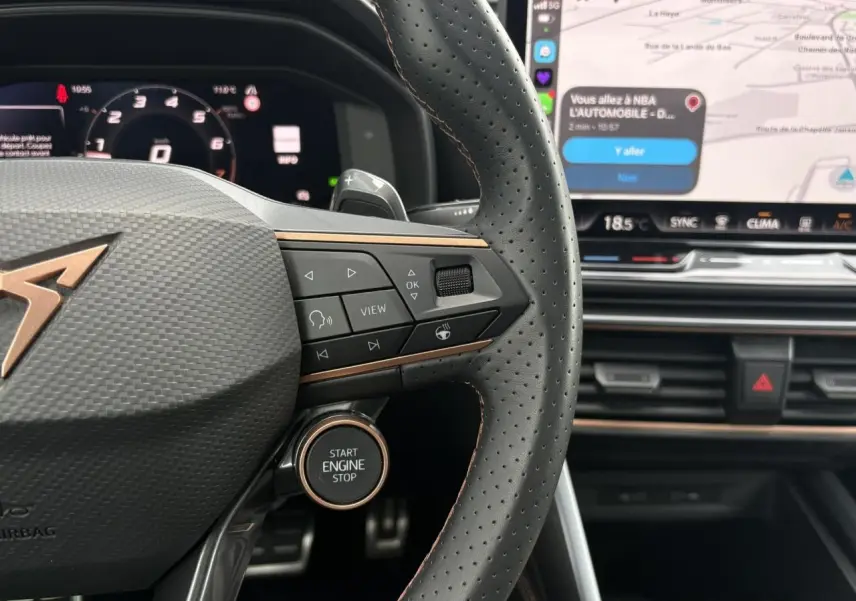 Gros plan sur le volant perforé noir avec logo CUPRA cuivré et bouton Start Engine, tableau de bord digital et écran tactile visible.