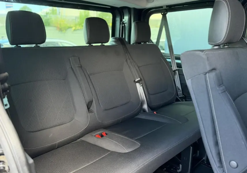 Vue intérieure sur la deuxième rangée de sièges noirs du Nissan Primastar Combi gris, avec ceintures et appuie-têtes visibles.