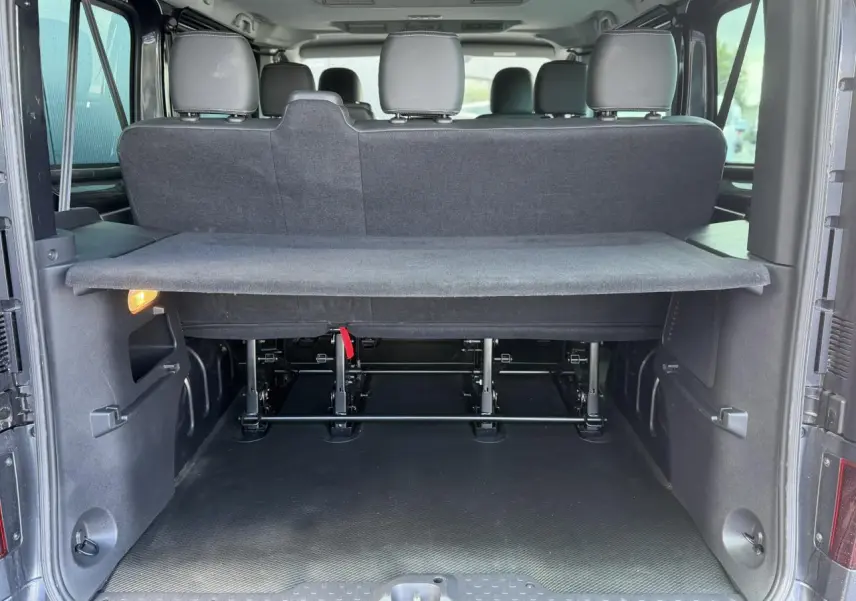 Vue arrière du Nissan Primastar Combi gris Comète montrant le hayon ouvert et l’espace de chargement avec cache-bagages.