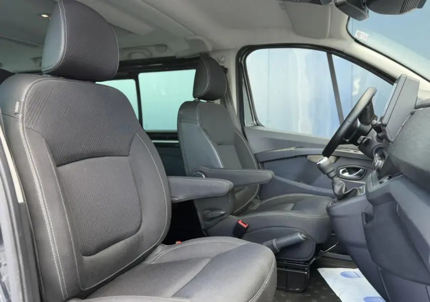Vue intérieure côté droit du Nissan Primastar Combi 2025, sièges avant gris foncé avec accoudoirs et volant visible.