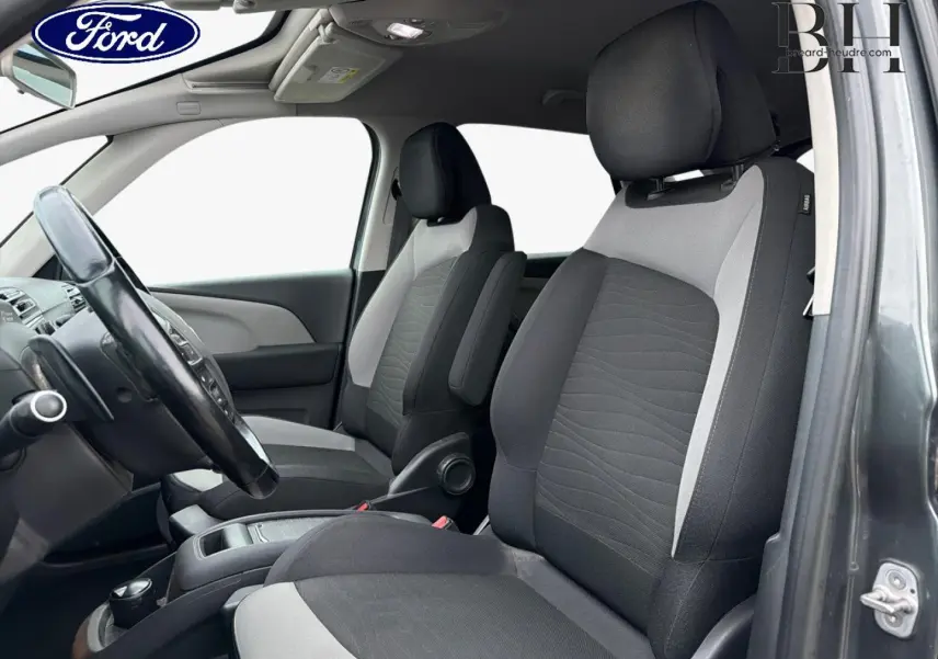 Vue intérieure côté conducteur de la Citroën C4 Picasso gris Shark, montrant les sièges avant en tissu bicolore noir et gris.