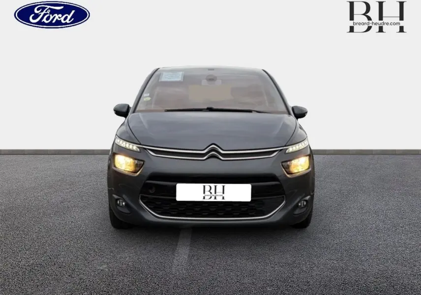 Vue de face d'une Citroën C4 Picasso gris Shark avec feux allumés sur un sol gris uniforme.
