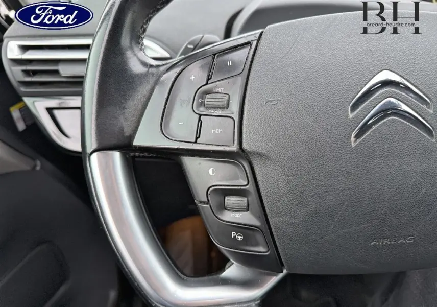 Gros plan sur le volant cuir gris avec commandes multifonctions et logo Citroën au centre, intérieur sombre.