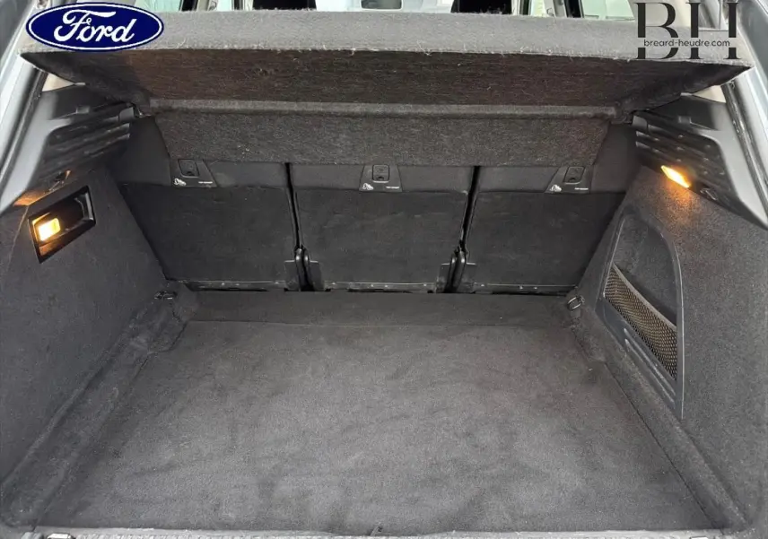 Coffre ouvert vu de l'arrière d'un Citroën C4 Picasso gris Shark avec habillage intérieur noir et éclairage latéral.