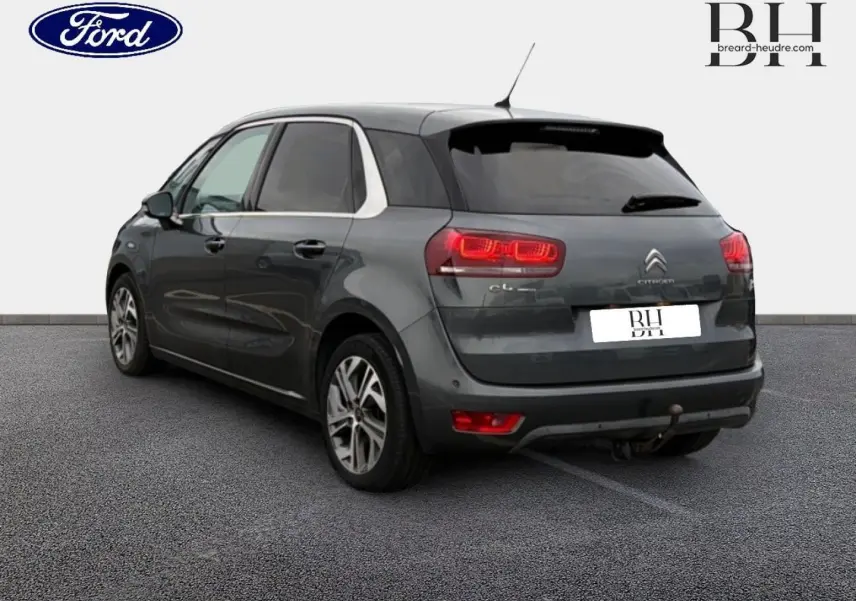 Citroën C4 Picasso gris Shark vue 3/4 arrière droit avec feux allumés et attelage visible.