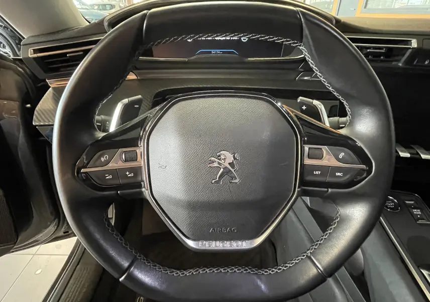 Gros plan sur le volant en cuir noir du Peugeot 508 2021, avec commandes intégrées et tableau de bord numérique en arrière-plan.