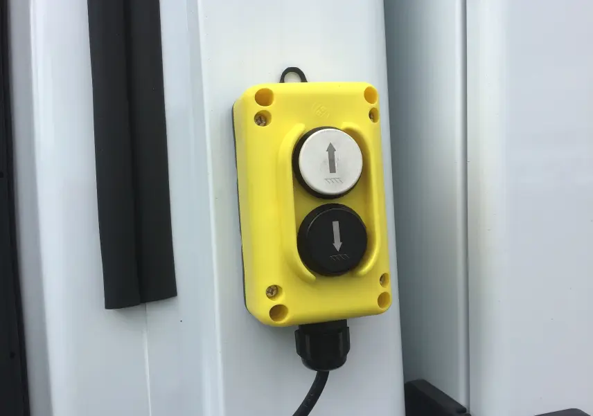 Gros plan sur un boîtier de commande jaune avec deux boutons fléchés sur la benne blanche du Ford Transit Chassis Cabine.