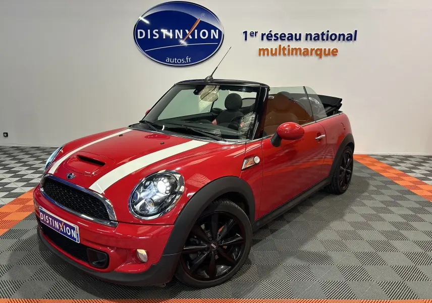 Vue 3/4 avant droite d'une MINI Cabriolet Cooper S rouge avec bandes blanches et jantes noires en intérieur showroom