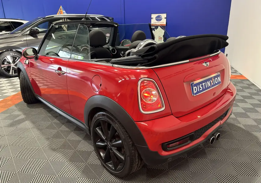 Vue arrière d'une MINI Cabriolet Cooper S rouge de 2012 avec capote noire repliée et double sortie d'échappement chromée.