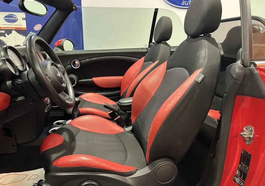 Intérieur côté gauche d'une MINI Cabriolet Cooper S rouge de 2012, sièges cuir rouge et noir, volant et levier manuel visibles.