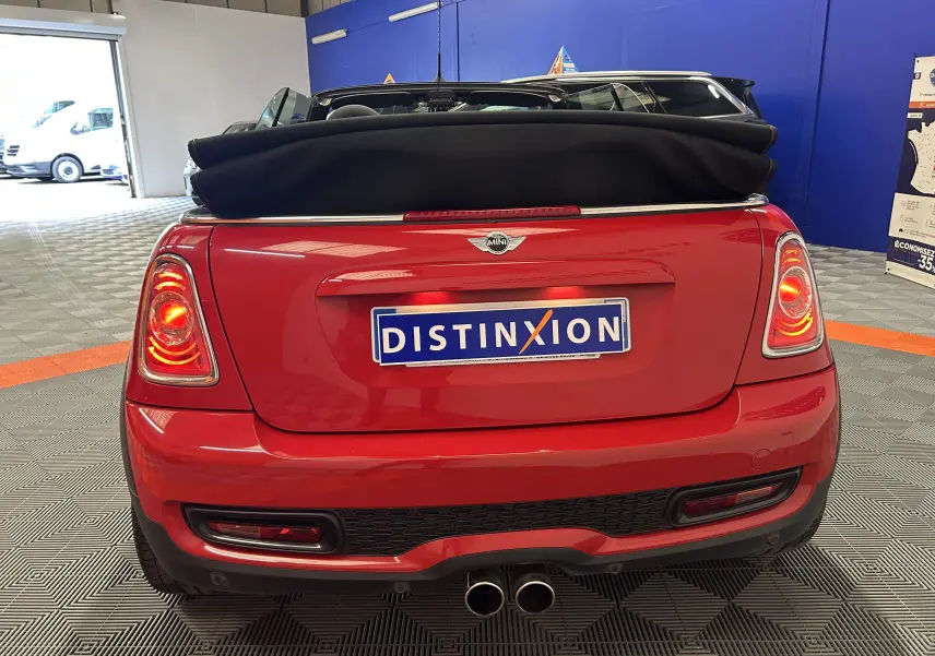 MINI Cabriolet Cooper S rouge vue 3/4 arrière droit, capote noire repliée, jantes noires et feux allumés.
