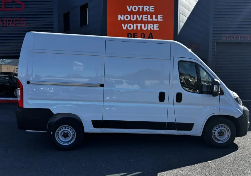Profil côté gauche d’un fourgon Peugeot Boxer blanc L2H2 2025 avec porte coulissante et protections noires basses.