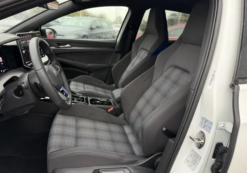 Vue intérieure côté conducteur de la Volkswagen Golf 1.5 eHybrid 2025 avec sièges sport à motif écossais et volant multifonction.