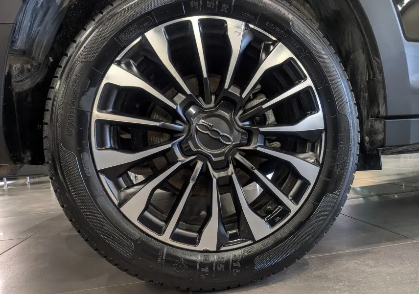 Gros plan sur la jante alliage bi-ton noire et argent du FIAT 500X 2024 Noir Cinéma, roue avant droite visible.