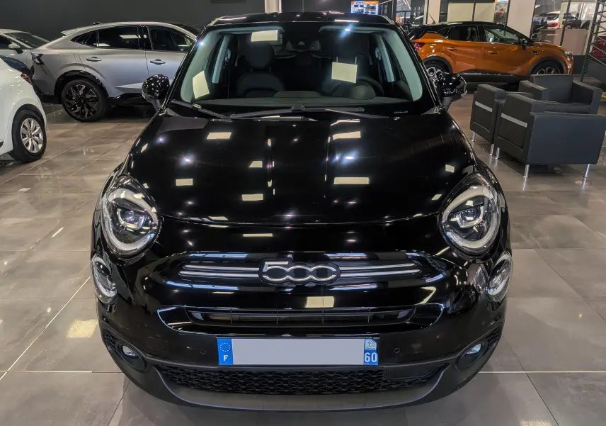 Vue frontale d'une FIAT 500X noire brillante exposée en showroom avec éclairage intérieur et sièges visibles.