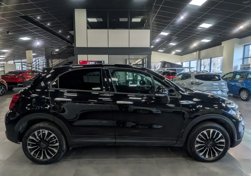 Vue de profil côté gauche d'une FIAT 500X noire Cinéma 2024 avec jantes alliage bicolores en showroom.