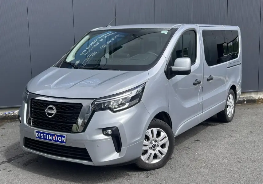 Nissan Primastar gris Highland vue 3/4 avant droit, hayon arrière vitré et vitres arrière surteintées visibles.