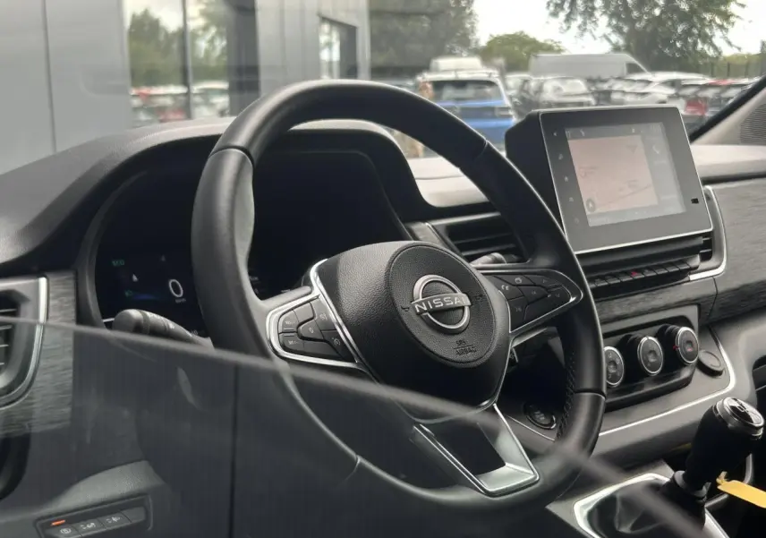 Vue intérieure centrée sur le volant Nissan et l'écran tactile du tableau de bord du Primastar gris Highland.