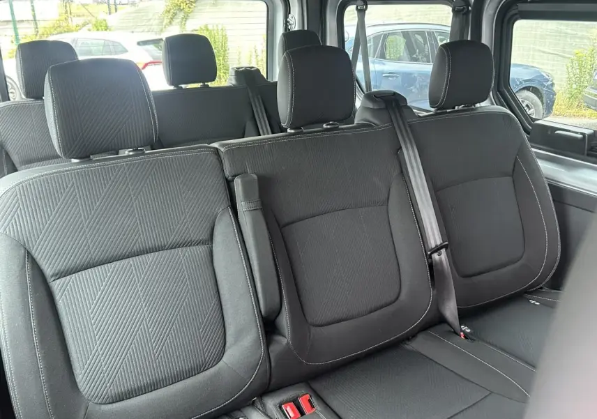 Vue intérieure sur les sièges arrière noirs du Nissan Primastar L1 3T 2.0 DCI 150 Tekna avec ceintures et appuie-têtes visibles.