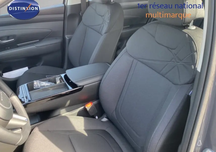 Vue intérieure rapprochée des sièges avant en tissu noir du Hyundai Tucson 2026 avec accoudoir central et console brillante.