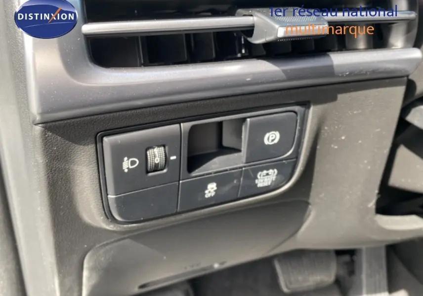 Détail des commandes côté gauche sous la ventilation du Hyundai Tucson gris Ecotronic 2026, avec boutons d'éclairage et frein à main électronique.