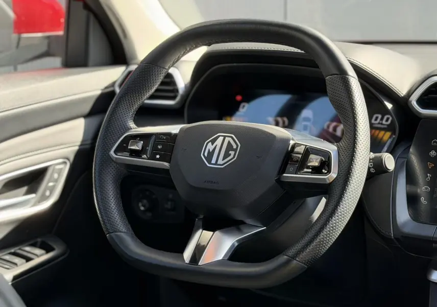 Gros plan sur le volant en cuir noir du MG ZS 1.5 Hybrid+ 197 Luxury, avec tableau de bord numérique en arrière-plan.