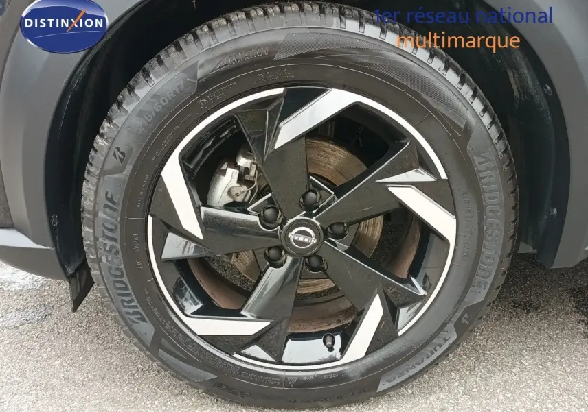 Gros plan sur la roue avant droite noire métallisée du Nissan Juke Hybrid 2024 avec jante alliage bicolore.
